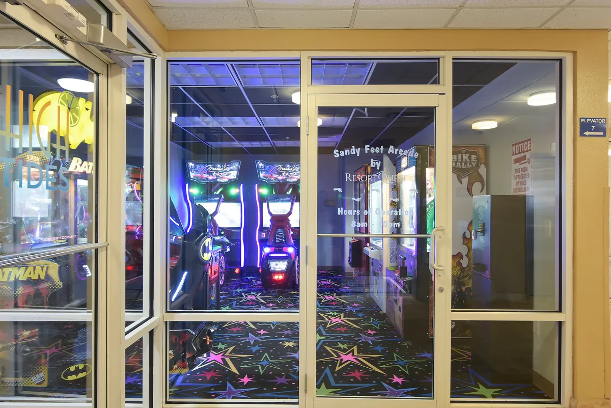 A vibrant interior arcade with colorful flooring, a lineup of arcade machines, and neon lights, where kids and families engage in games and entertainment.
