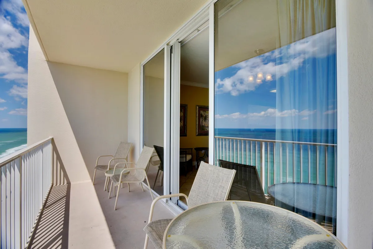 This image captures a tranquil balcony scene overlooking the ocean. The space is furnished with a glass table and chairs, inviting guests to sit back and relax while soaking in the unobstructed water views. The balcony's rail offers a clear, sweeping view of the Gulf, with the horizon visible in the background and gentle waves below.