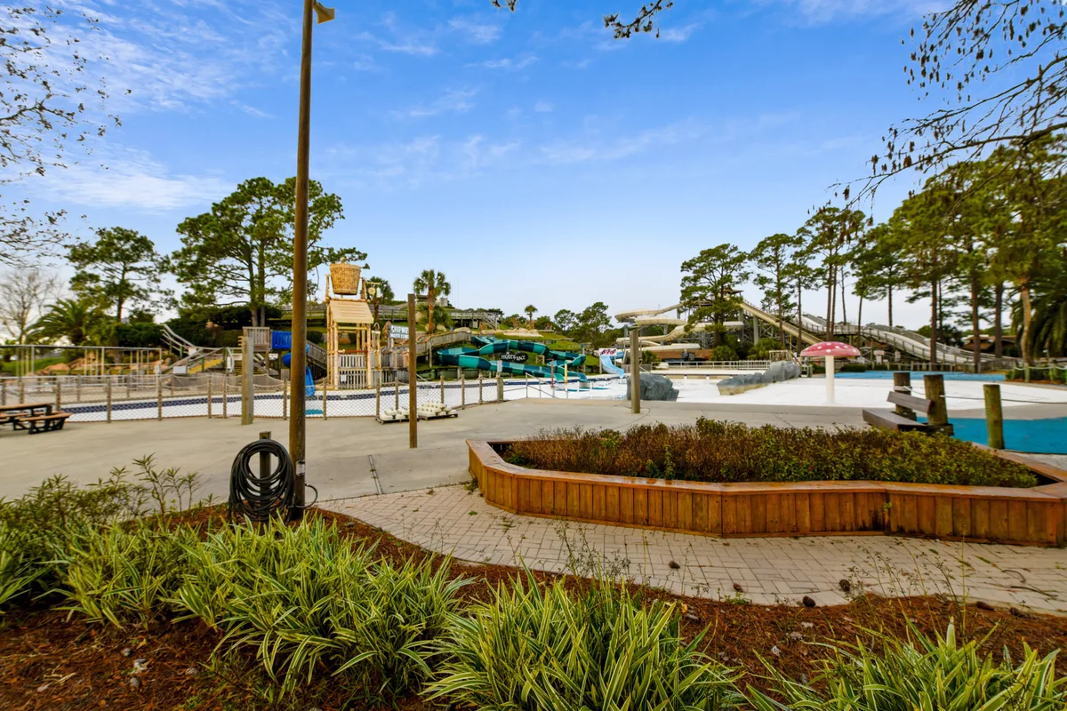 An energetic scene at Shipwreck Island Water Park, featuring colorful water slides, a sparkling pool, a playground area, and landscaped gardens. Families and children are actively engaged in swimming, sliding, and relaxing in the sun, creating an atmosphere of excitement and togetherness.