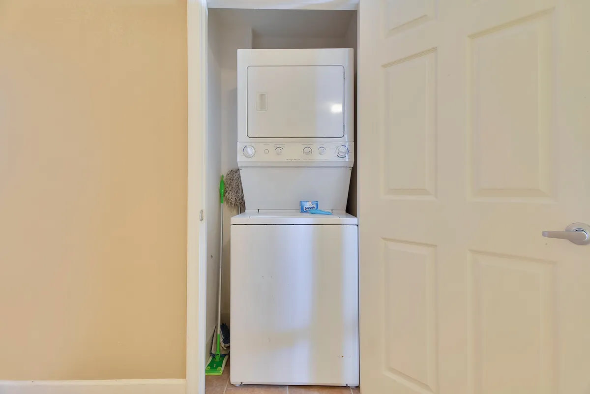 A stacked washer and dryer with cleaning supplies arranged nearby, suggesting practical in-unit laundry for effortless stays.
