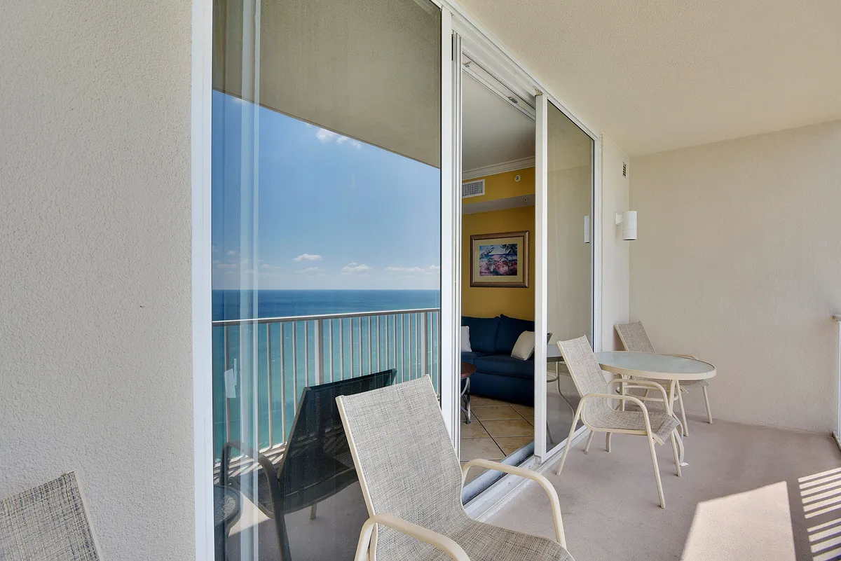 A view from the balcony looking outward toward the ocean, with comfortable balcony furniture and a glimpse of the interior seating area through glass doors. The photo highlights the seamless transition between indoor and outdoor living, which is a major feature of the section.