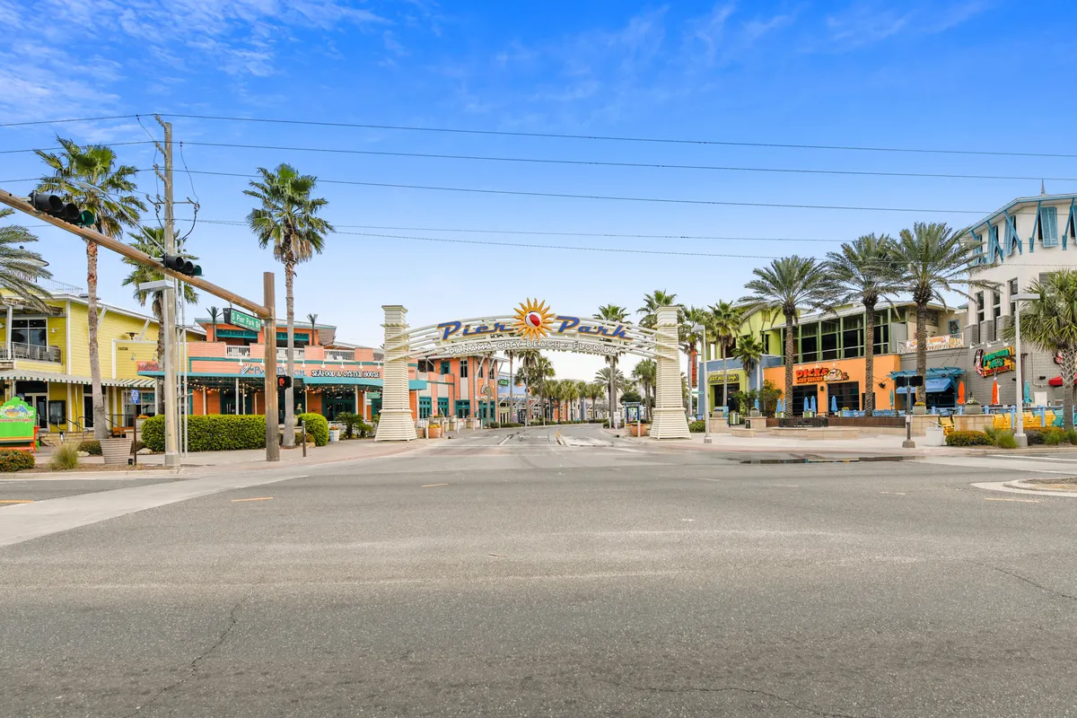 This image captures the lively entrance archway to a shopping and entertainment district, with colorful buildings and palm trees lining the sidewalks. People are seen strolling, shopping, and dining, creating a cheerful and bustling atmosphere perfect for social outings.