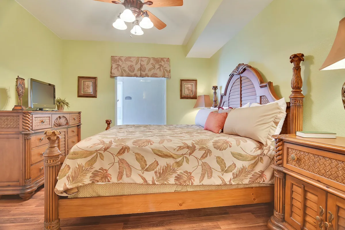 A king bedroom featuring a bed with floral bedding, wooden furniture, and a television on a dresser. Lamps on nightstands cast a soft, serene glow, inviting relaxation and comfort.
