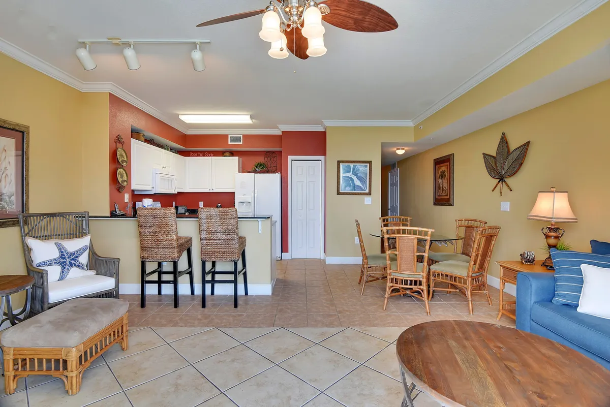 A cozy living and dining area with a blue sofa, wooden dining table, and a kitchen bar area. Warm accents and decorative wall art create a welcoming atmosphere, making it an inviting hub for relaxing, sharing meals, or playing games with loved ones.