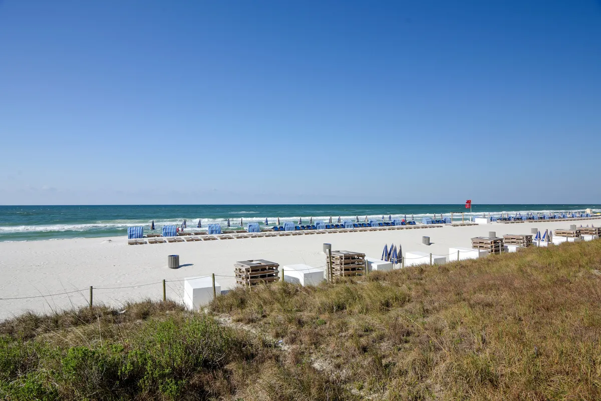 A tranquil beachfront scene with rows of beach chairs and umbrellas set on the sandy shore, the blue ocean waves gently rolling in the background, and dunes providing a picturesque foreground. The overall mood is peaceful and inviting, perfect for groups to gather and enjoy the waterfront together.