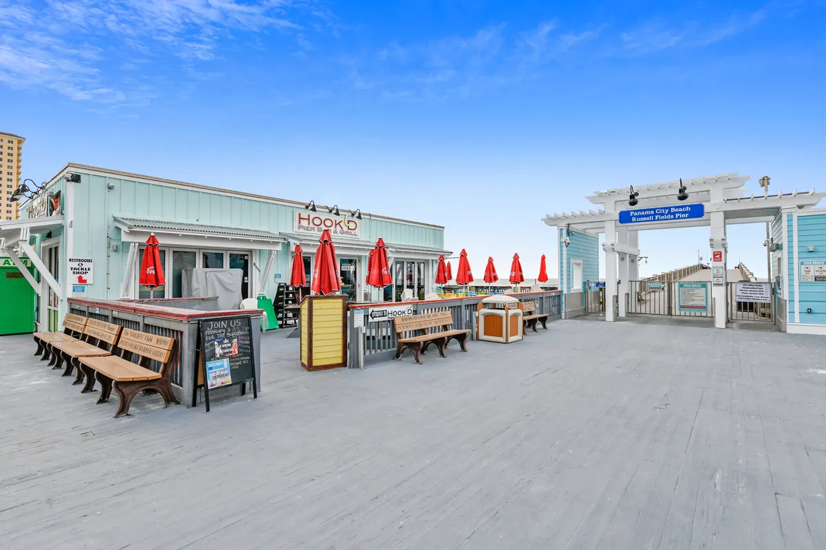 The inviting HookD restaurant with red umbrellas and a lively boardwalk area, set against the entrance to Panama City Beach. People are dining outdoors, enjoying both the atmosphere and proximity to the beach.